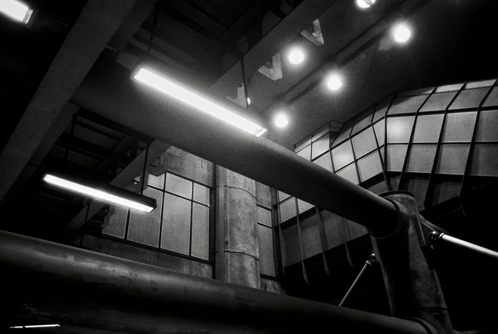 A black and white photograph of the interior of Westminster underground station, looking up from the mezzanine level at the escalators. An ethereal look with the halos around the lights.